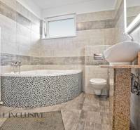 A bathroom in a family house with a bathtub, sink, and toilet, tiled with light tiles.