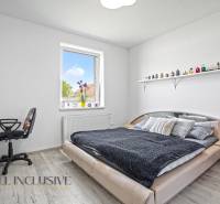 A bedroom in a family house with a bed, a chair, a table, and a shelf on the wall.