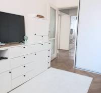 White living room in a 4-room apartment with a TV, cabinets, and wooden flooring.