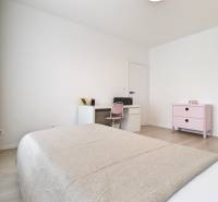 A bright bedroom with a bed, table, and dresser in a 3-room apartment.
