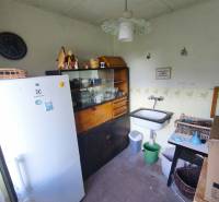 A kitchenette in a cottage with a sink, refrigerator, display cabinet, and a clock on the wall.