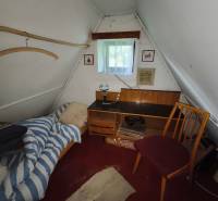 Attic room in a cottage with a bed, table, and chair, white wall.