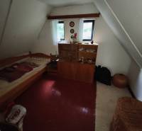 Attic room in a cottage with a bed, cabinet, and floor with wooden decor.