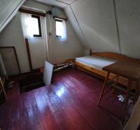 A room on the upper floor in a cottage with a wooden decor floor, simple furniture, and windows.
