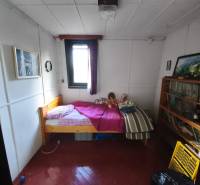 A room in a cottage with a bed, a bookshelf, and art pictures on the walls.