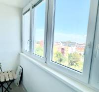 A glazed balcony with a view of Bratislava, a potted plant, a chair, and a table.