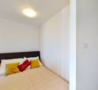 A bedroom with a double bed, white walls, and colorful pillows in a studio apartment.