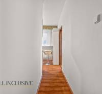 A narrow hallway in a 2-room apartment with wooden flooring and light-colored furniture.