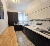 A kitchen with dark furniture, a cooktop, and a sink in a 3-room apartment.