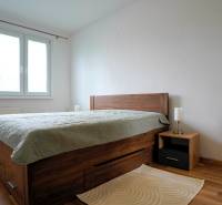 Bedroom in a two-room apartment with wooden flooring and a bed with storage space.