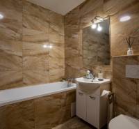 Bathroom in a family house with a bathtub, sink, and beige tiles in warm tones.