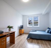 A room in a family house with a bed, a desk, and a television on a light floor.