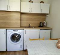 A kitchen in a studio apartment with white cabinets, a washing machine, a sink, and a dining table.