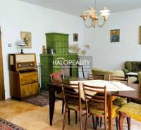 Living room in a family house with wooden furniture, a green tiled stove, and paintings on the walls.
