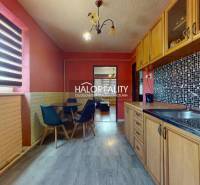 A kitchen in a 2-room apartment with a wooden cabinet, a round table, and a brick wall.