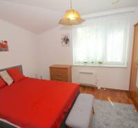 A bedroom in a family house with red bedding, a dresser, and a large window.