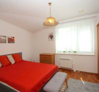 A bedroom in a family house with a double bed, wooden furniture, and red accessories.