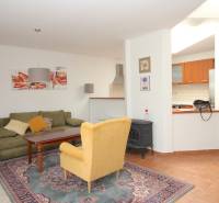 Living room with a carpet, green sofa, yellow armchair, and a kitchenette in a family house.