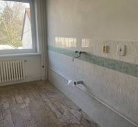 An empty kitchen in a family house with tiles and wooden flooring.