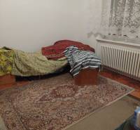 A room in a family house with a bed, carpet, and lace curtains.
