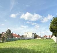 Land for residential use in Sládkovičovo, grass, fences, trees, buildings in the background, cloudy sky.