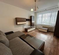 1-bedroom apartment with a sofa, wooden furniture, and a large window with a lace curtain.