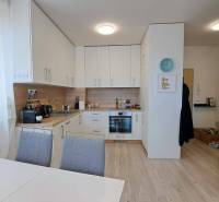 A kitchen in a 2-room apartment with a white kitchenette, dining table, and wooden floor.