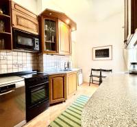 A kitchen in a 2-room apartment with wooden furniture, a stove, a microwave, and a dishwasher.