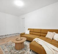A room in a 3-room apartment with a brown sofa, a table, and a patterned carpet.