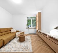 Living room in a three-room apartment with a brown sofa, a table, and a large window.