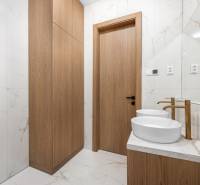 A bathroom with two sinks, wooden cabinets, and marble tiles in a three-room apartment.