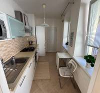 A kitchen in a 2-room apartment with white cabinets and windows with blinds.