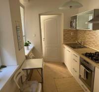 A kitchen in a 2-room apartment with light furniture, appliances, and a dining table.