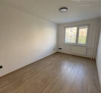 An empty room with a wooden floor in a 3-room apartment, a large window and a radiator under it.