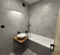 A bathroom in a 3-room apartment with a bathtub and a sink on a wooden countertop.