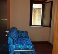 A blue sofa by an open window in a three-room apartment with wooden flooring.