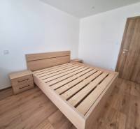 A bedroom with a wooden bed in a two-room apartment, without a mattress and with a nightstand.