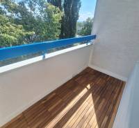 A balcony with a wooden floor and a view of trees in a 2-room apartment.