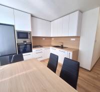 A kitchen in a 2-room apartment with modern furniture, appliances, and a dining table.