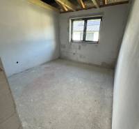 Unfinished room in a family house with a window and exposed roof beams.