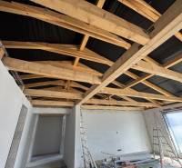 The family house has white plaster, wooden beams, and an unfinished ceiling.