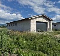 An unfinished family house in Valča surrounded by lush vegetation and a mountainous backdrop.
