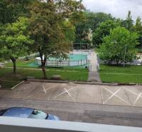 View from a 3-room apartment in Bratislava - Ružinov on Mesačná Street, parking lot, trees, and playground.