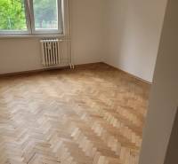 A room in a 3-room apartment with wooden parquet floors, a large window, a radiator underneath it.
