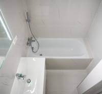 A bathroom with a bathtub, a sink, and a mirror in a 2-room apartment.