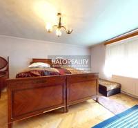 The interior of a cabin with a wooden bed, a tiled stove, and a carpet.