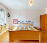 A bedroom in a family house with a wooden floor, a bed, and a window with a view of the garden.