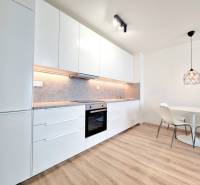 The kitchen of a 3-room apartment with white furniture and a round table with chairs.