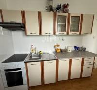 A kitchen in a 2-room apartment with white cabinets and a stove with a hood.
