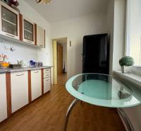 A kitchen in a 2-room apartment with a glass table and white cabinets.